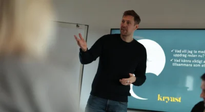 Man presenterar vid stor skärm och håller ut handen.