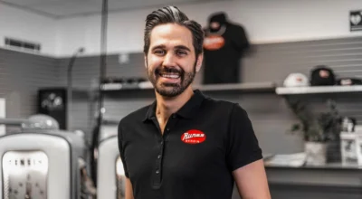 Man i svart piké tittar in i kameran och ler