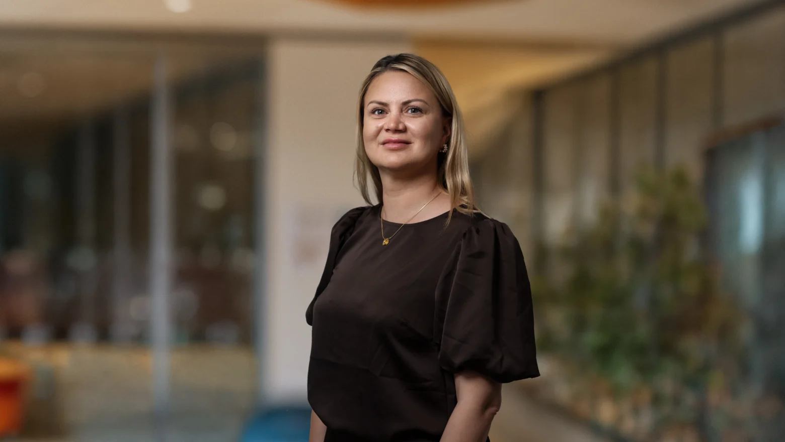 Kvinna med brun blus tittar in i kameran och ler